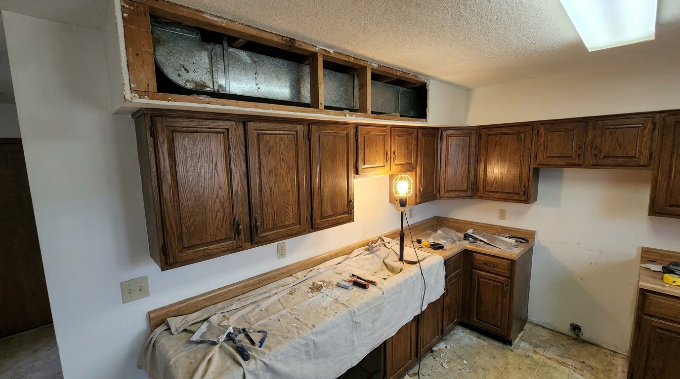 Kitchen soffit above old wall cabinets opened up during demolition, showing a metal duct running inside the drywall box